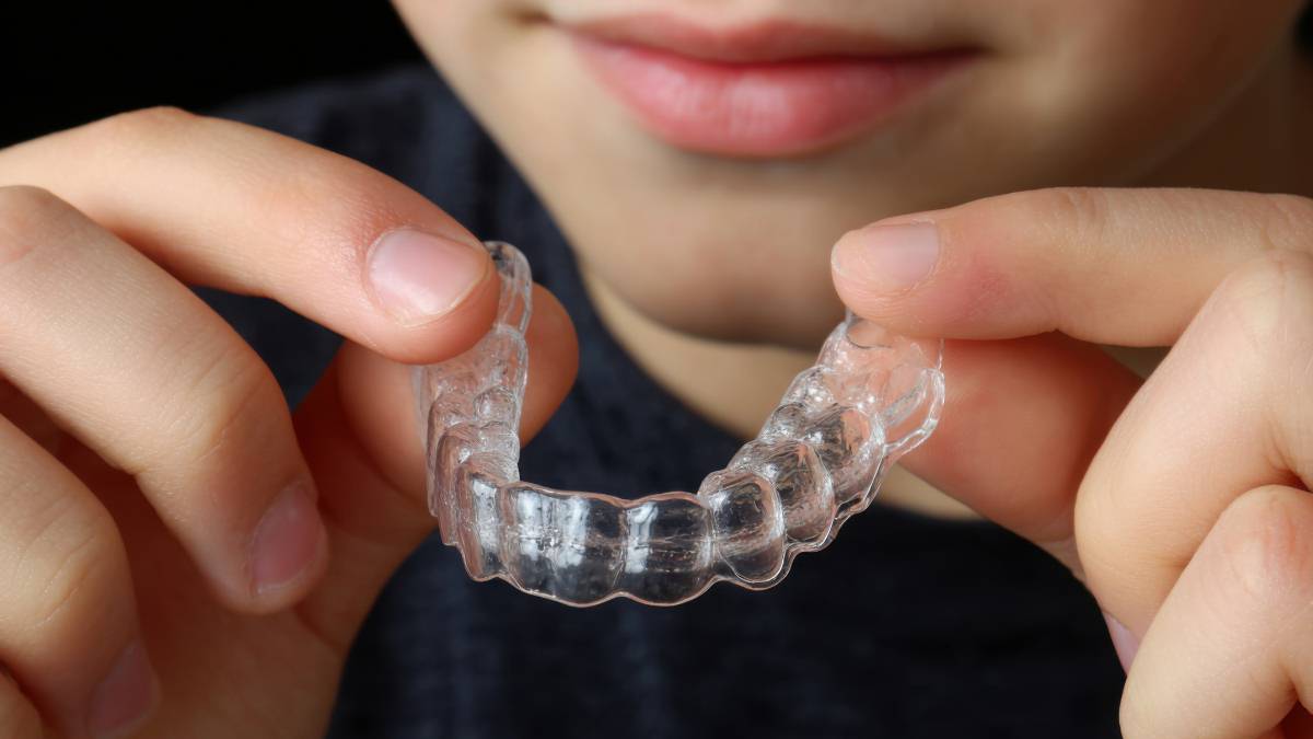 Sakarya çocuk diş hekimliğinde şeffaf plak (telsiz tedavi) kullanan genç bir hastanın elinde tuttuğu şeffaf düzeltici plak detay görünümü